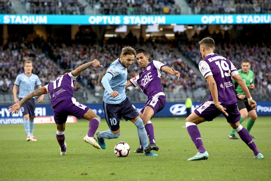 Three Perth defenders surround Milos Ninkovic, who maintains control of the ball.