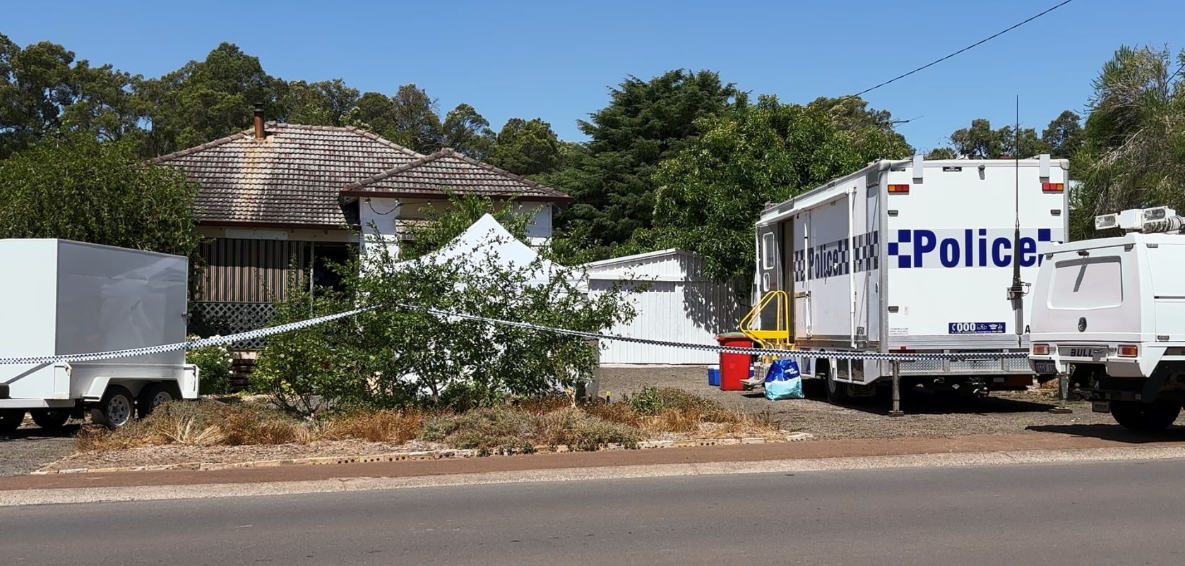 Police banner cordoning off a house with police van and equipment in front yard