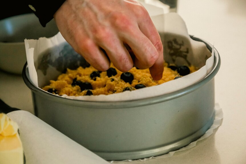 A close up of a man's hand inside a cake tin filled with batter.