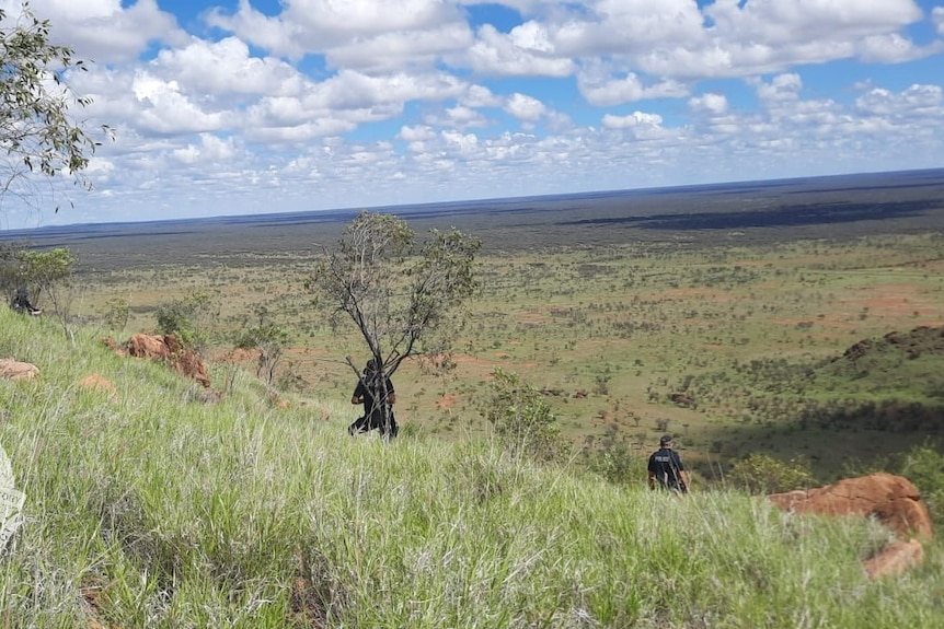 Two police officers can be seen walking over hill terrain in Central Australia