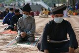 Men wearing traditional Malay attire and face masks sit in a socially-distanced manner at a mosque