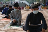 Men wearing traditional Malay attire and face masks sit in a socially-distanced manner at a mosque