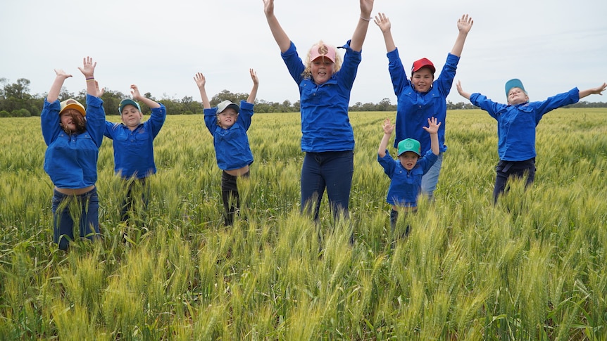 Seven primary school kids jumping happily in a wheat paddock.