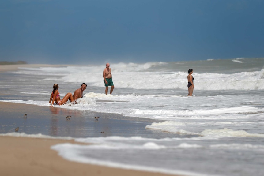 Four people play in choppy surf at a beach.