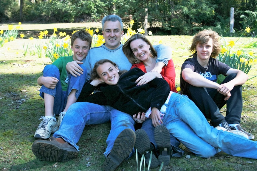 A man in his fifties sitting with his wife and three children in a forest.