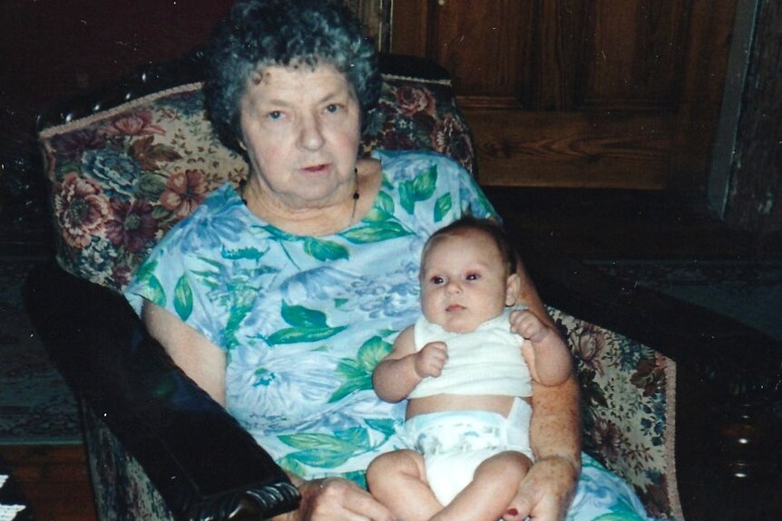 An elderly baby sitting in an arm chair holding a baby