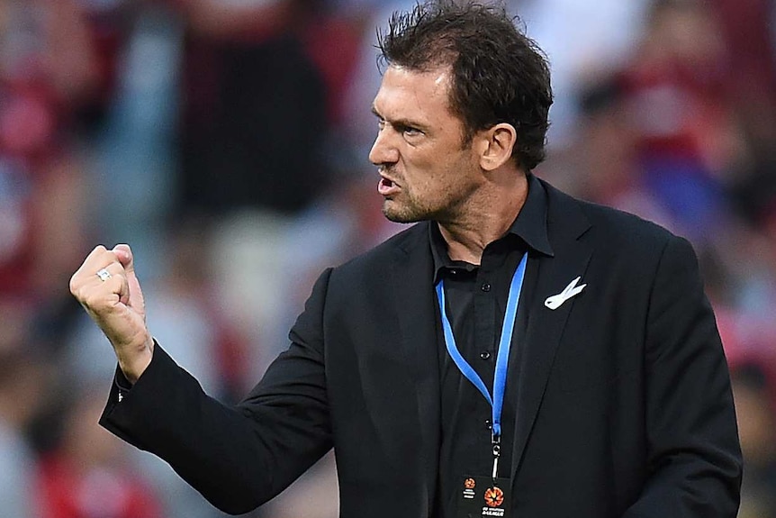 A mid-shot of Tony Popovic pumping his fist on the sideline during an A-League game.