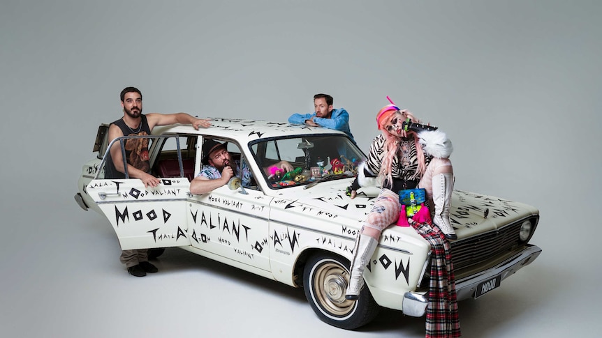 The four members of Hiatus Kaiyote sit on and around an old white car which is painted with words