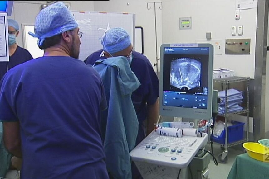 A group of surgeons in blue scrubs examine a patient with an ultrasound machine. 