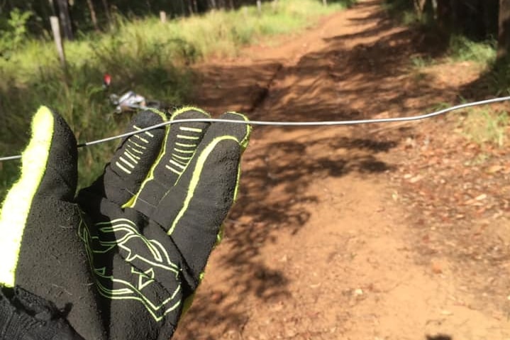 Gloved hand holds up metal wire strung up across dirt path