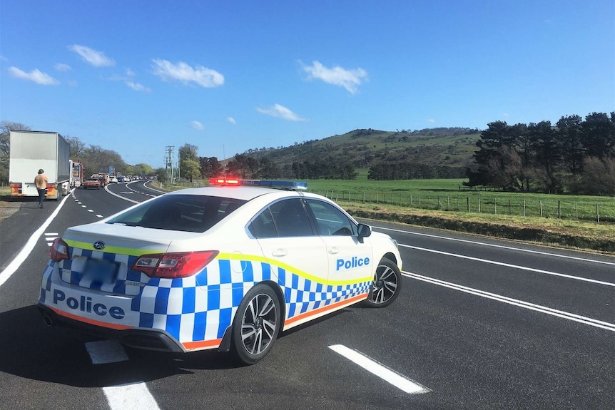 A police car is parked across a highway with its lights on and traffic queuing in the distance.