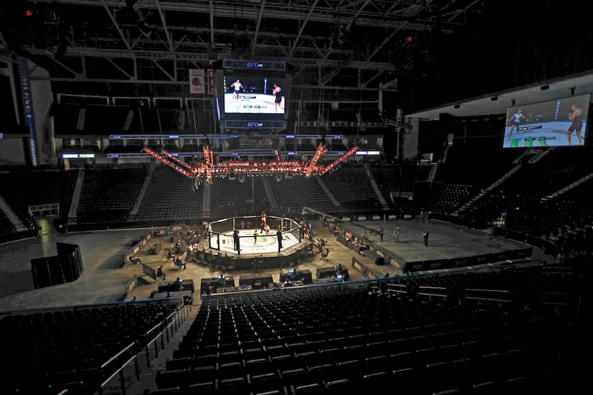 A long-distance shot of two MMA fighters in a cage, surrounded by empty seats.