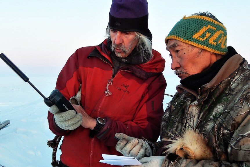 Two men look at a radio in the Arctic.