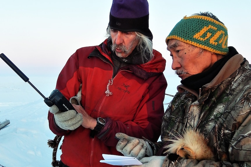 Two men look at a radio in the Arctic.