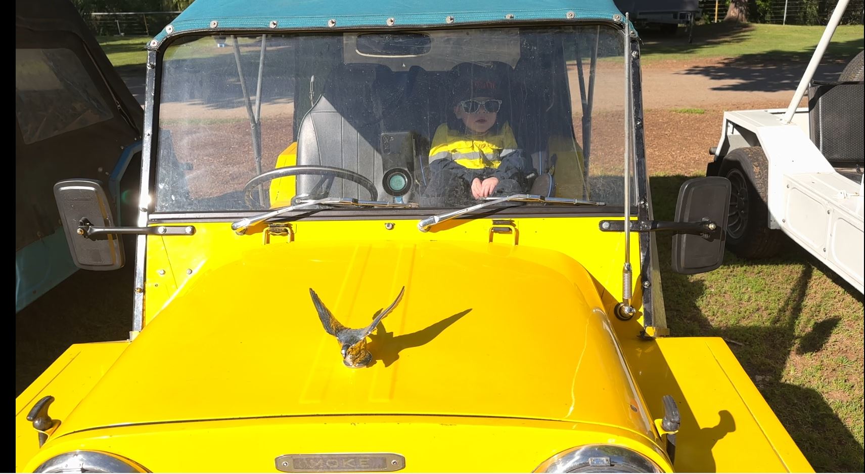 A bright yellow Mini Moke with a young child in the passenger seat.