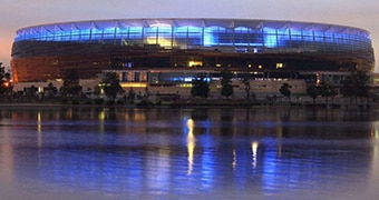 Perth Stadium illuminated at twilight and reflected in the Swan River.