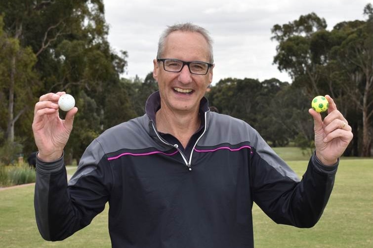 Golfer Jim Grant on a golf course, smiling and holding up two golf balls.