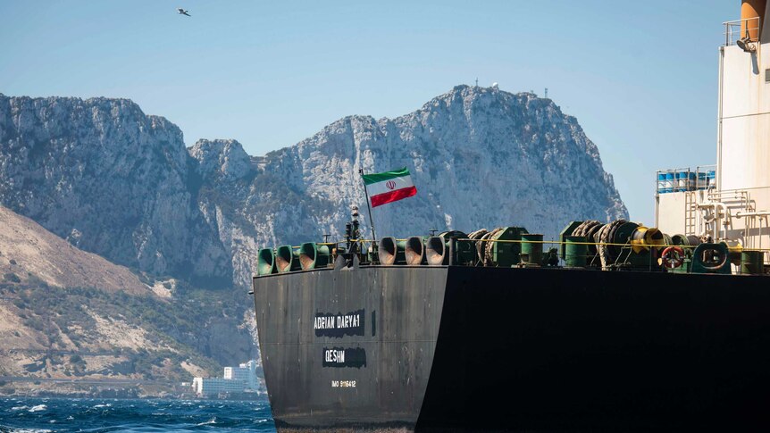 An Iranian flag flies on the deck of a supertanker with mountains seen behind.