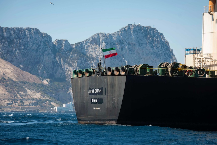 An Iranian flag flies on the deck of a supertanker with mountains seen behind.