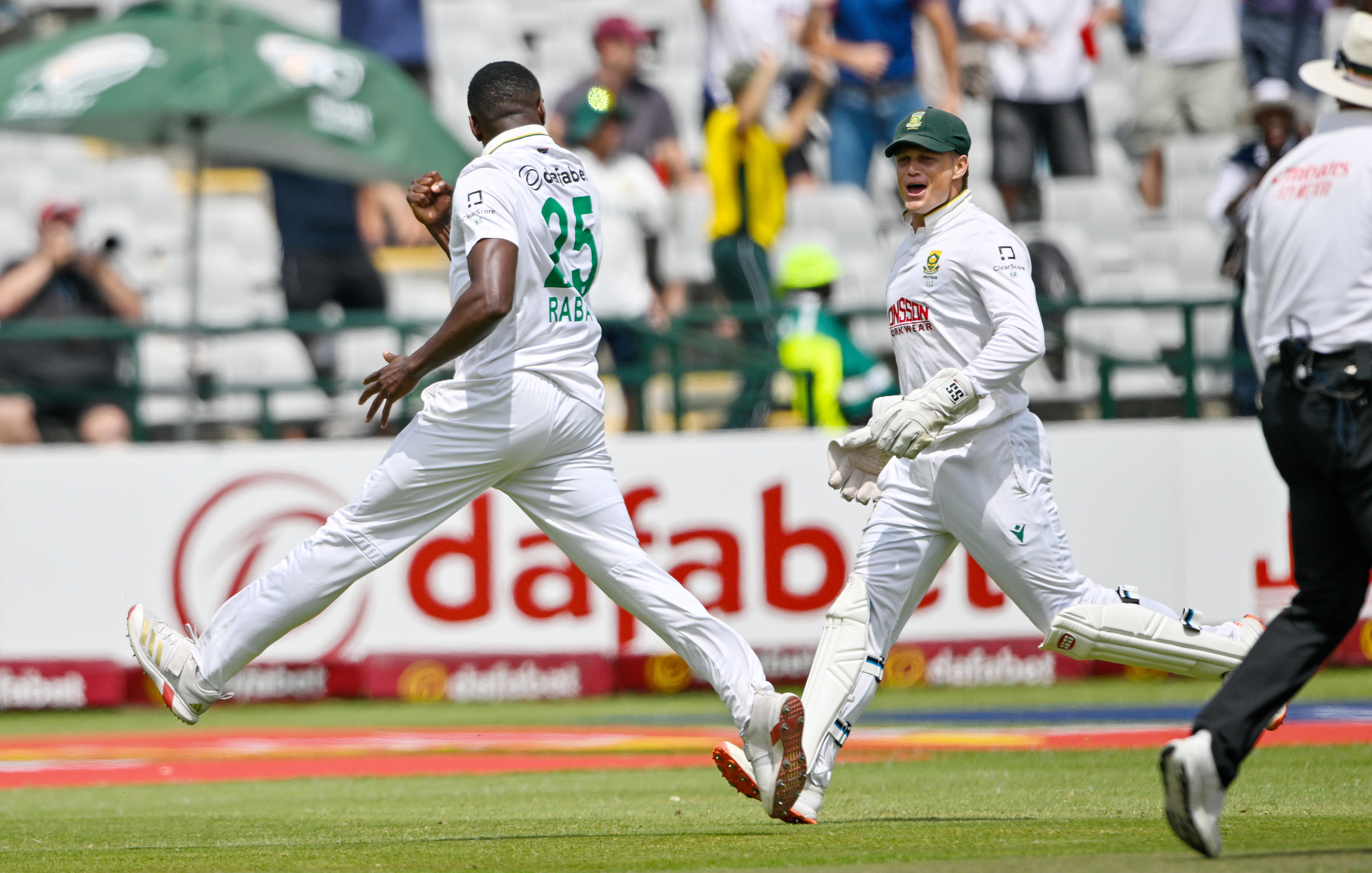 A South African pace bowler runs away after taking a wicket, as his teammate grins in celebration.