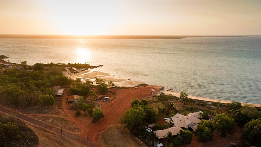 An aerial view of a setting sun on a small settlement next to a tropical bay