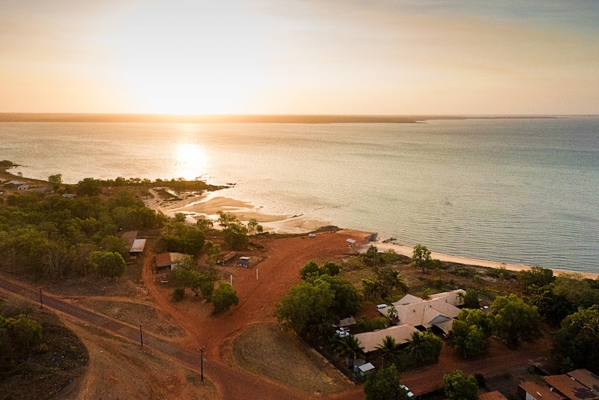 An aerial view of a setting sun on a small settlement next to a tropical bay