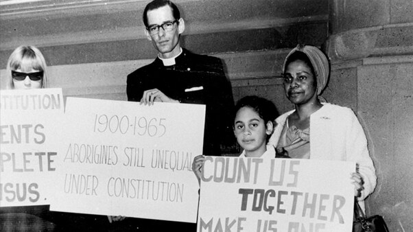 Four people stand holding signs, one of which reads 'count us together, make us one people'.