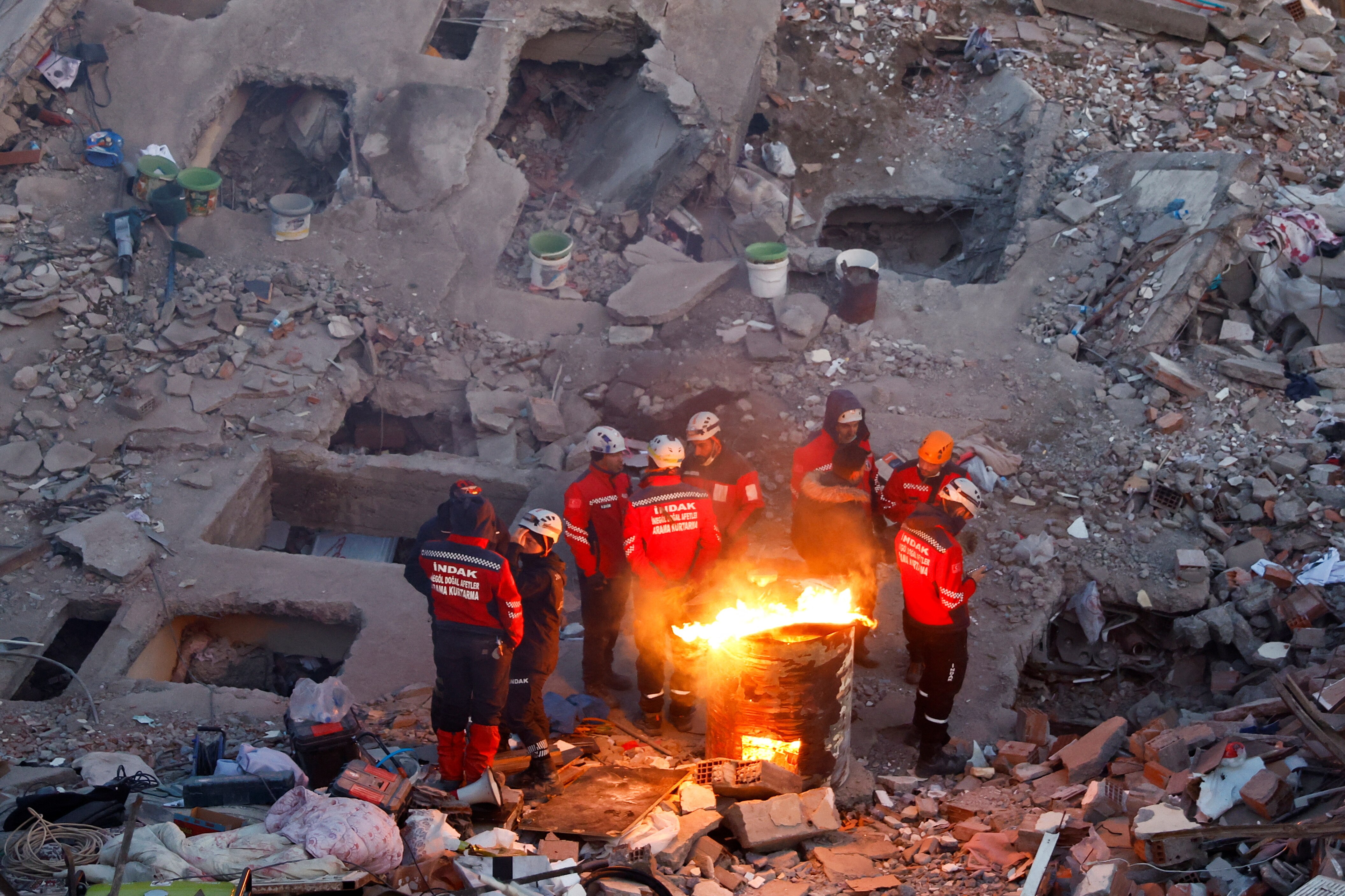 Emergency workers huddle around fire at site of collapsed building.