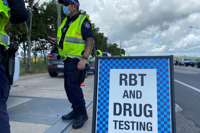 An officer standing by a sign that advisers drivers of RBT and drug testing