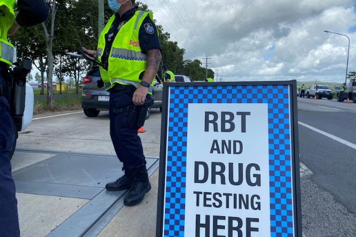 A sign advising drivers RBT and Drug Testing here and an officer standing near it