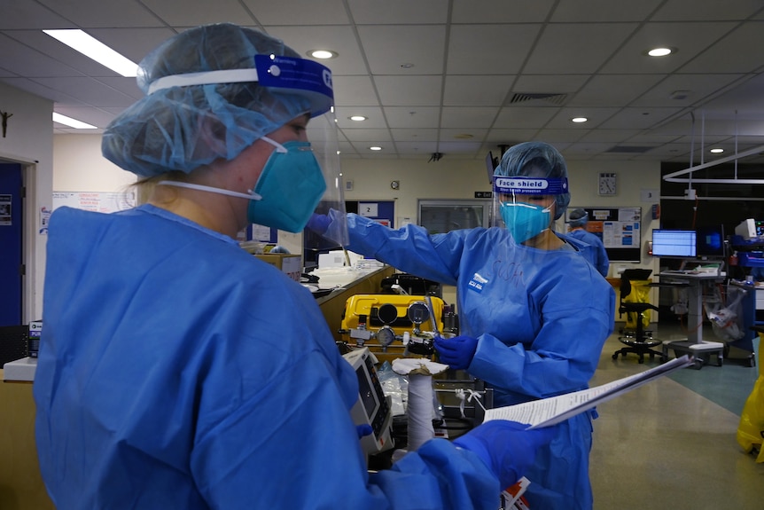 Two people in full PPE speaking to each other.