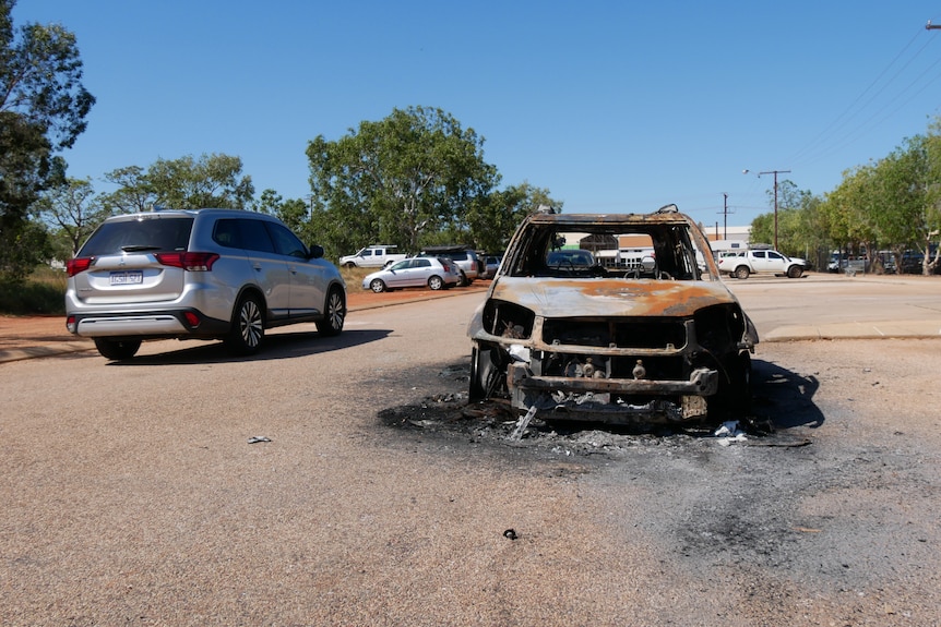 A torched car sits in the middle of a road in an outback town.