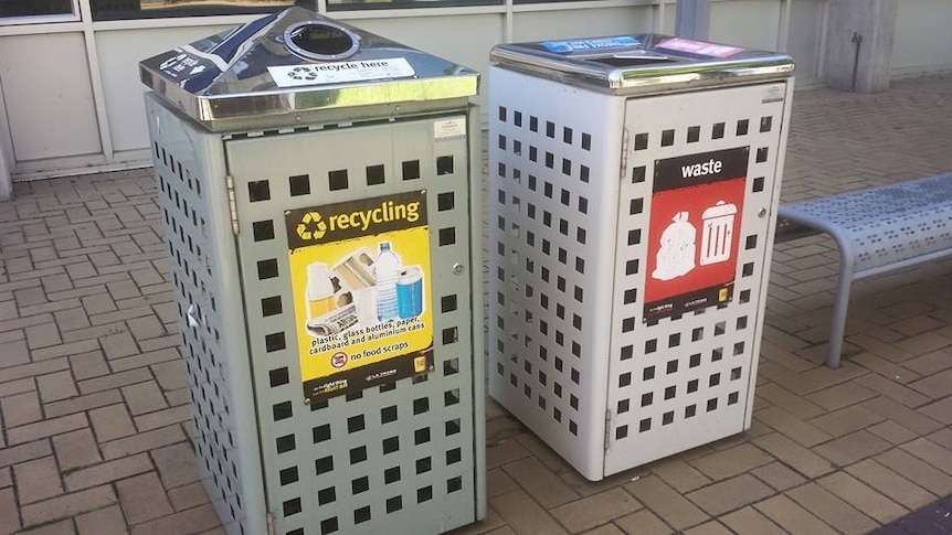 Metal encased bins with a yellow sign for recycling and a red sign for waste
