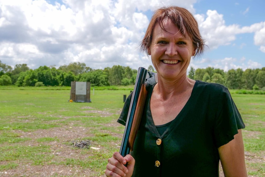 Lil Brandt smiles at the camera with a gun over her shoulder.