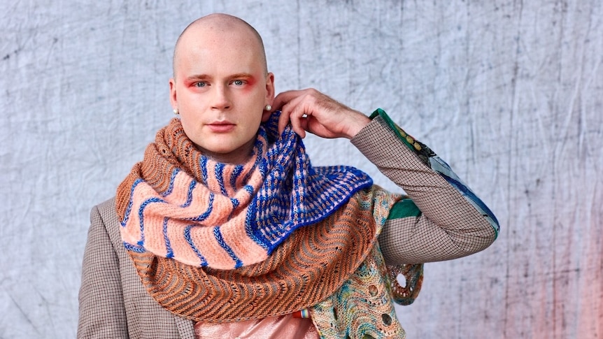 a man looks at the camera with a knitted shawl around his neck