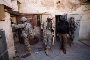 Three men in military fatigues, one in plain clothes in a stone courtyard