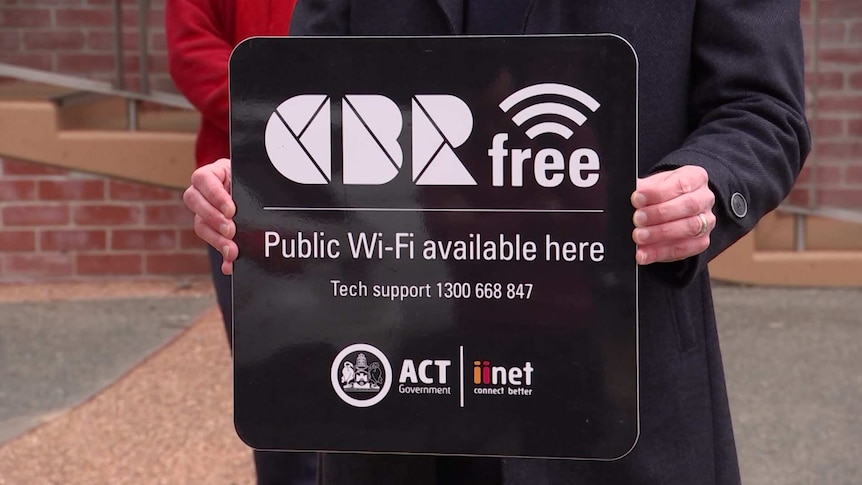 A man holds a sign that reads 'CBRfree Public Wi-Fi available here'.