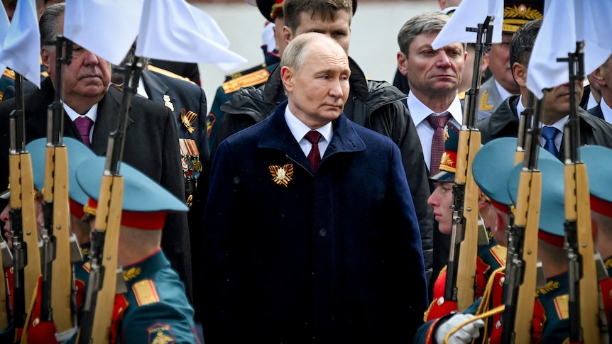 A man in a dark coat stands among a military parade