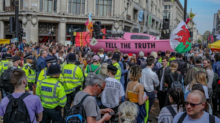 A large group of protesters block traffic while waving flags as police watch on.