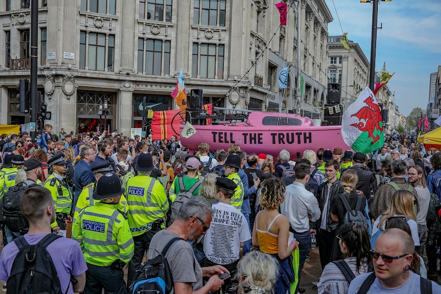 A large group of protesters block traffic while waving flags as police watch on.