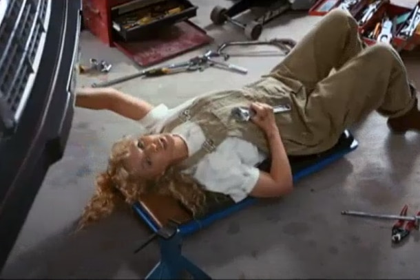 Kylie wearing khaki overalls and a white shirt as she lies on a trolley