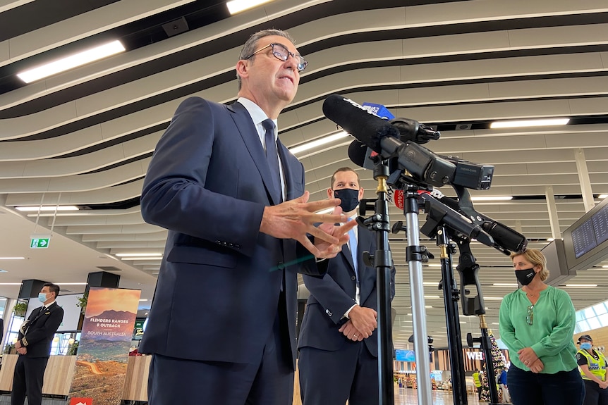 A man wearing a suit and tie speaks to microphones