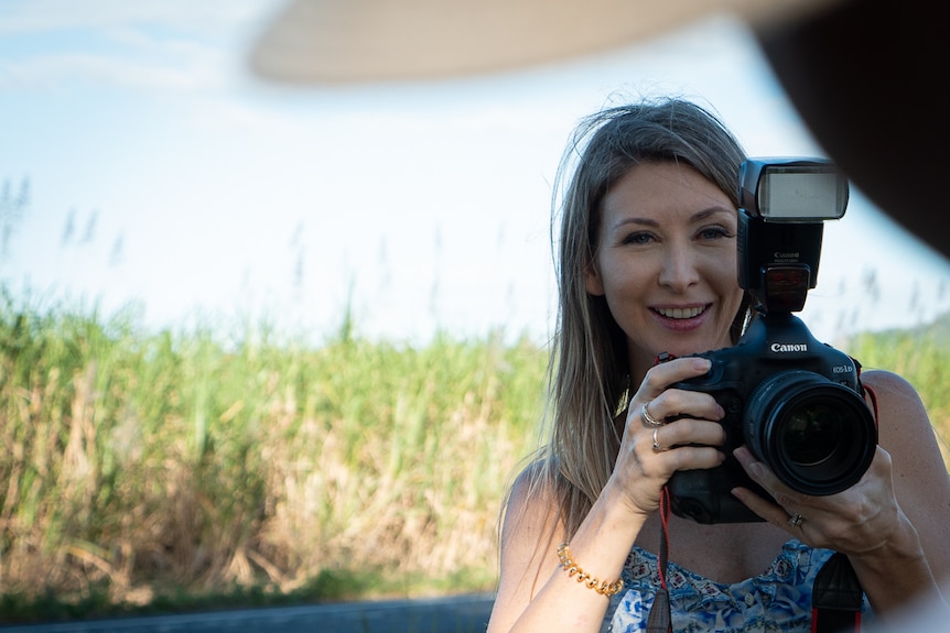 Woman holding camera standing by highway and canefield