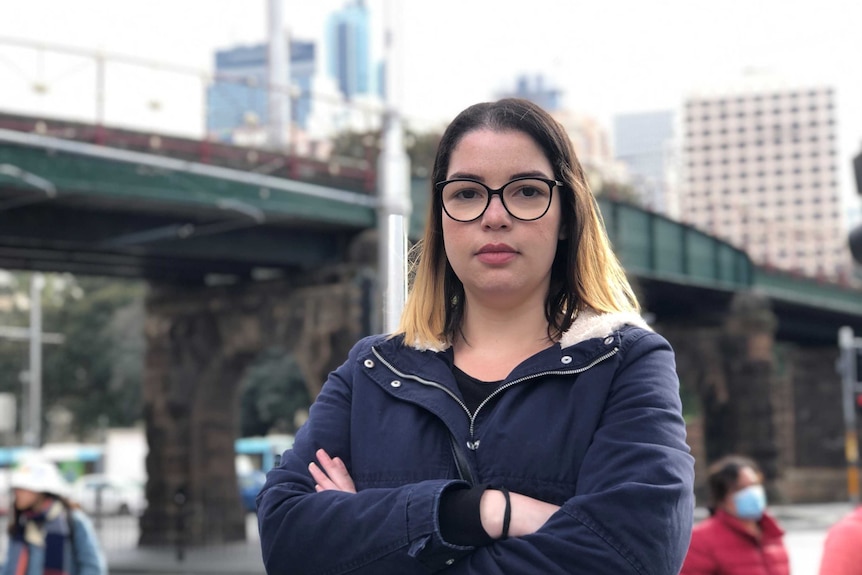 Renata Tavares Silva, an international student, with her arms crossed standing on the street as pedestrians walk by.