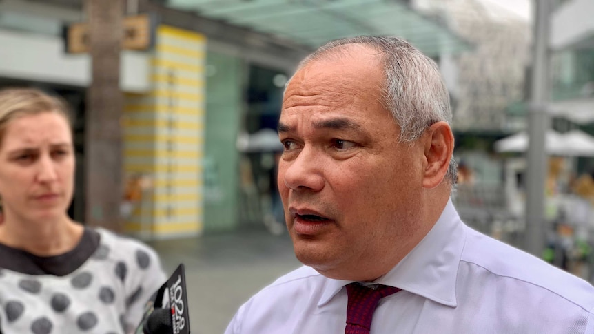 A man wearing a red tie talks to media