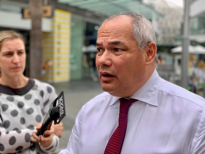 A man wearing a red tie talks to media