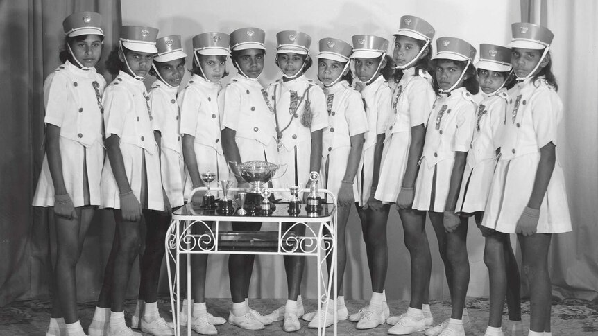 A black and white photo of Indigenous girls in the Cherbourg marching girls with their trophies in Melbourne 1962.