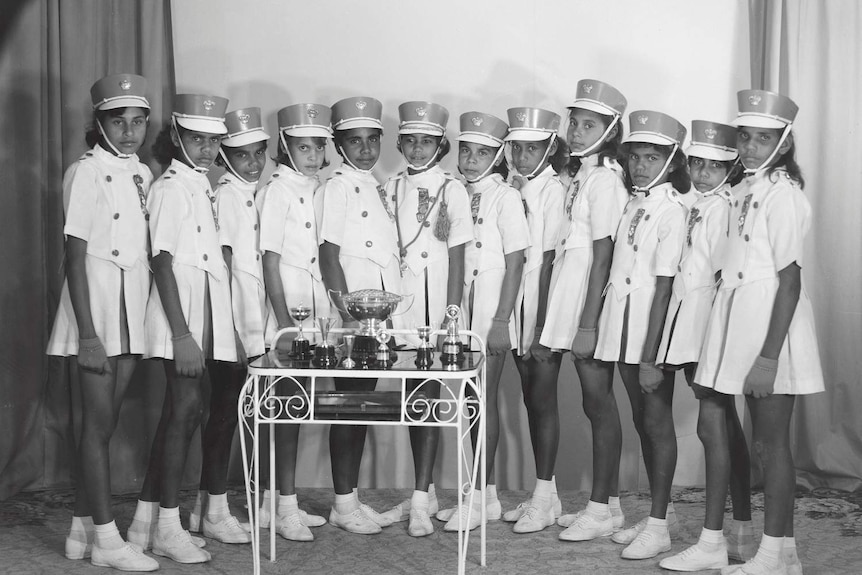 A black and white photo of Indigenous girls in the Cherbourg marching girls with their trophies in Melbourne 1962.