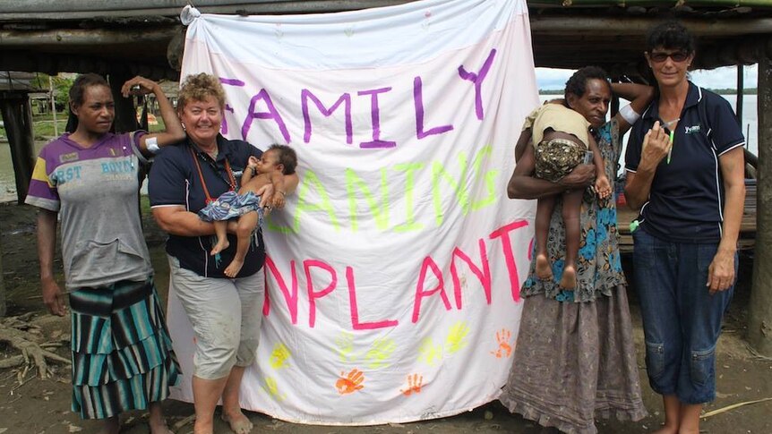 Four people, one holding a baby and one holding a child, stand in front of a family planning banner.