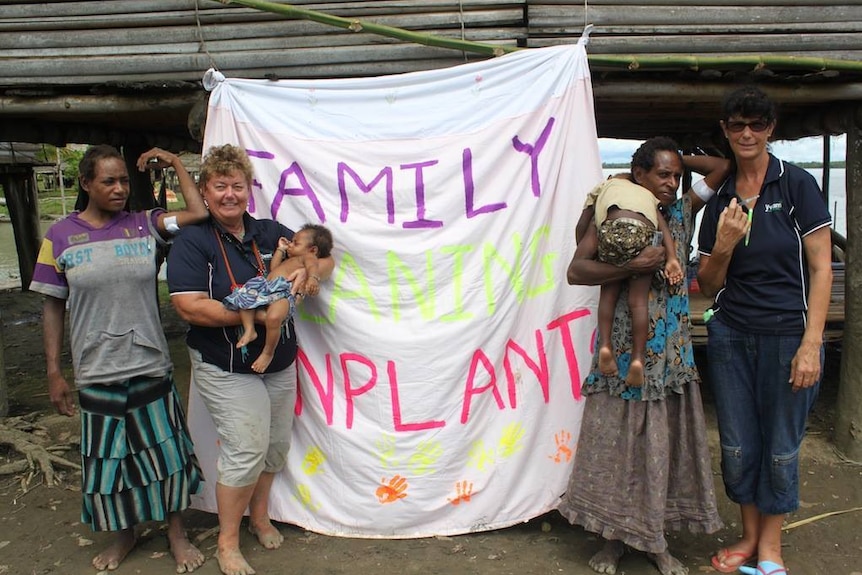 Four people, one holding a baby and one holding a child, stand in front of a family planning banner.